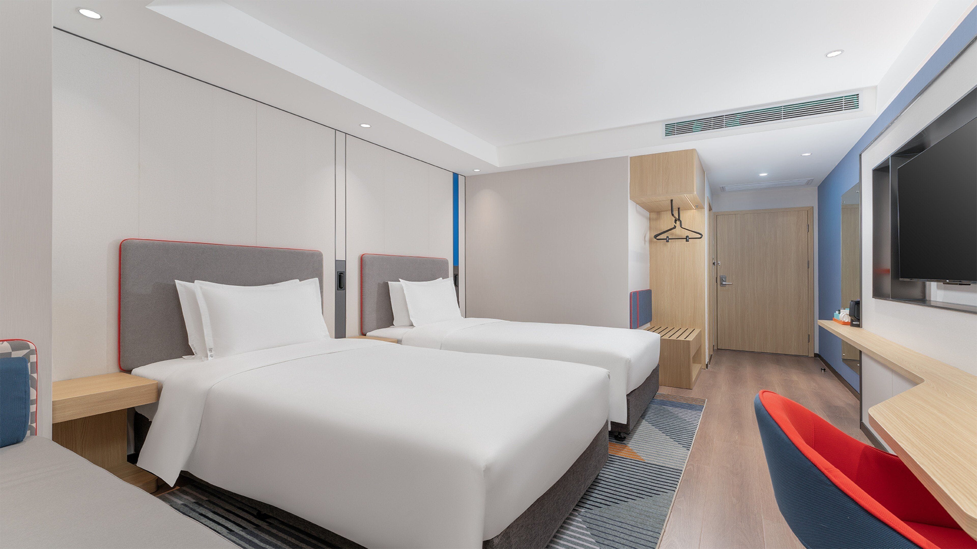 A hotel room with two beds, a TV, a desk, and a bathroom.