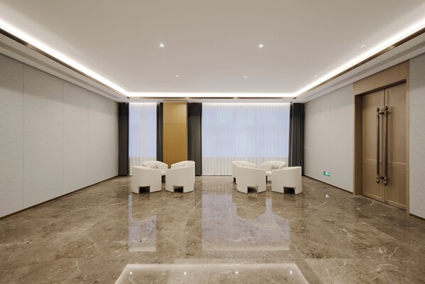 A spacious, modern room with a polished marble floor, a seating area with white chairs, and a large wooden door.