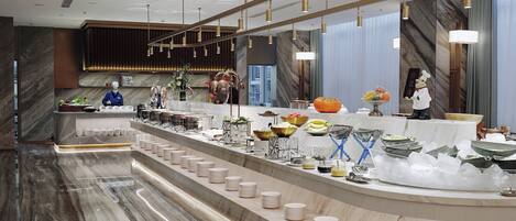 A modern hotel lobby with a marble reception desk, a buffet area, and a large mirror reflecting the space.