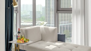 Une chambre moderne avec un canapé-lit, une petite table sur laquelle se trouvent une bouteille et des fruits, et une lampe.