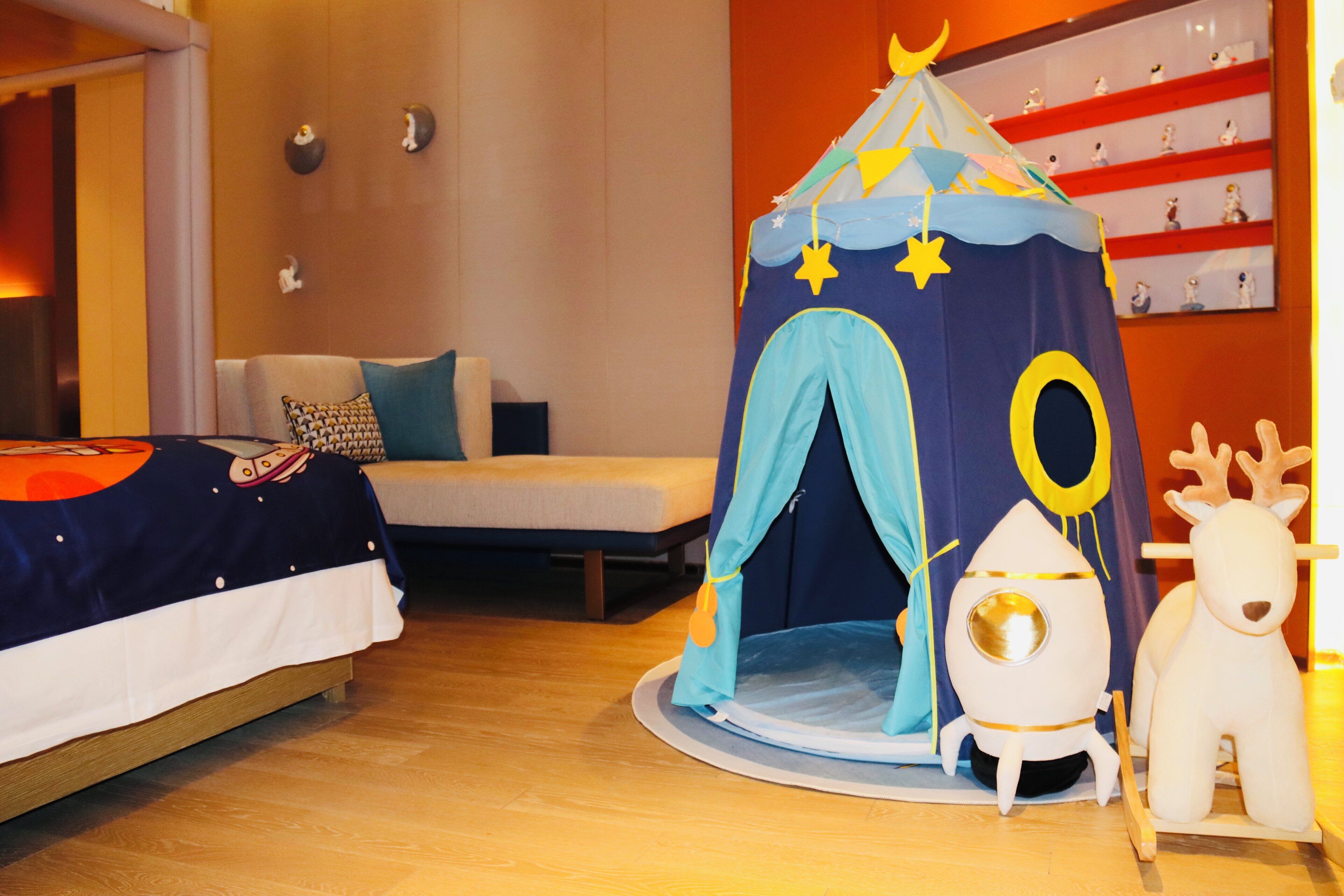 A child's play tent with stars and a moon, a plush reindeer, and a bed with a colorful blanket.