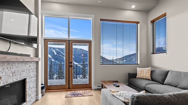 A modern living room with a fireplace, a sofa, a coffee table, and large windows with a mountain view.