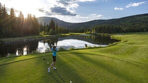 A golf course with a pond, trees, and a mountain in the background.