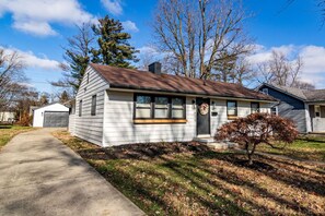 A single-story house with a front porch, a garage, and a small yard with a tree.
