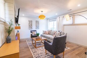 Una sala de estar con un sofá, un sillón, una mesita de centro y un televisor montado en la pared.