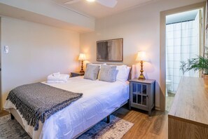A bedroom with a bed, bedside lamps, a painting, and a view of the bathroom.