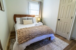 Una cama bien hecha con un edredón marrón, una lámpara de noche y una ventana con cortinas.