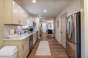 A modern kitchen with stainless steel appliances, white cabinetry, and a wooden floor.