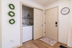A laundry room with a washer and dryer, a clock on the wall, and a door leading to another room. - Hamilton Modern Organic 3Bed 3Bath Noblesville (Noblesville)