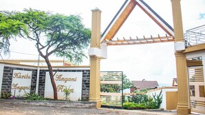 Uma entrada com portão, estrutura de telhado triangular, uma árvore e uma placa com a inscrição "Karibu Angani Resort".