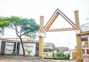 Una entrada protegida por una reja con una estructura de techo triangular, un árbol y un cartel que dice "Karibu Angani Resort".