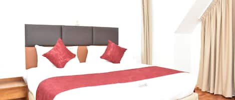 A neatly made bed with a white and red bedspread, two red pillows, and a dark headboard.
