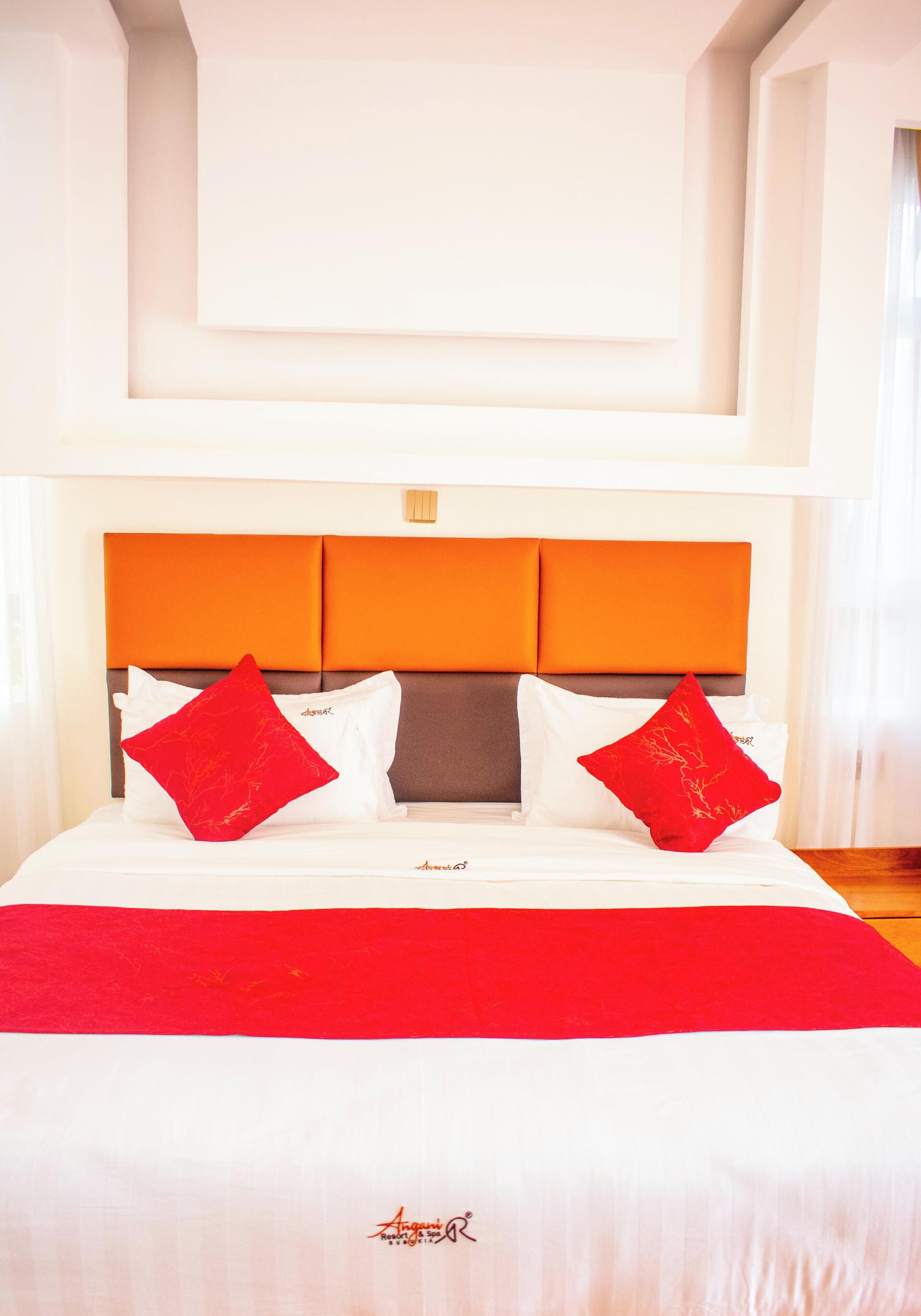 A hotel room with a large bed, orange headboard, and red pillows.