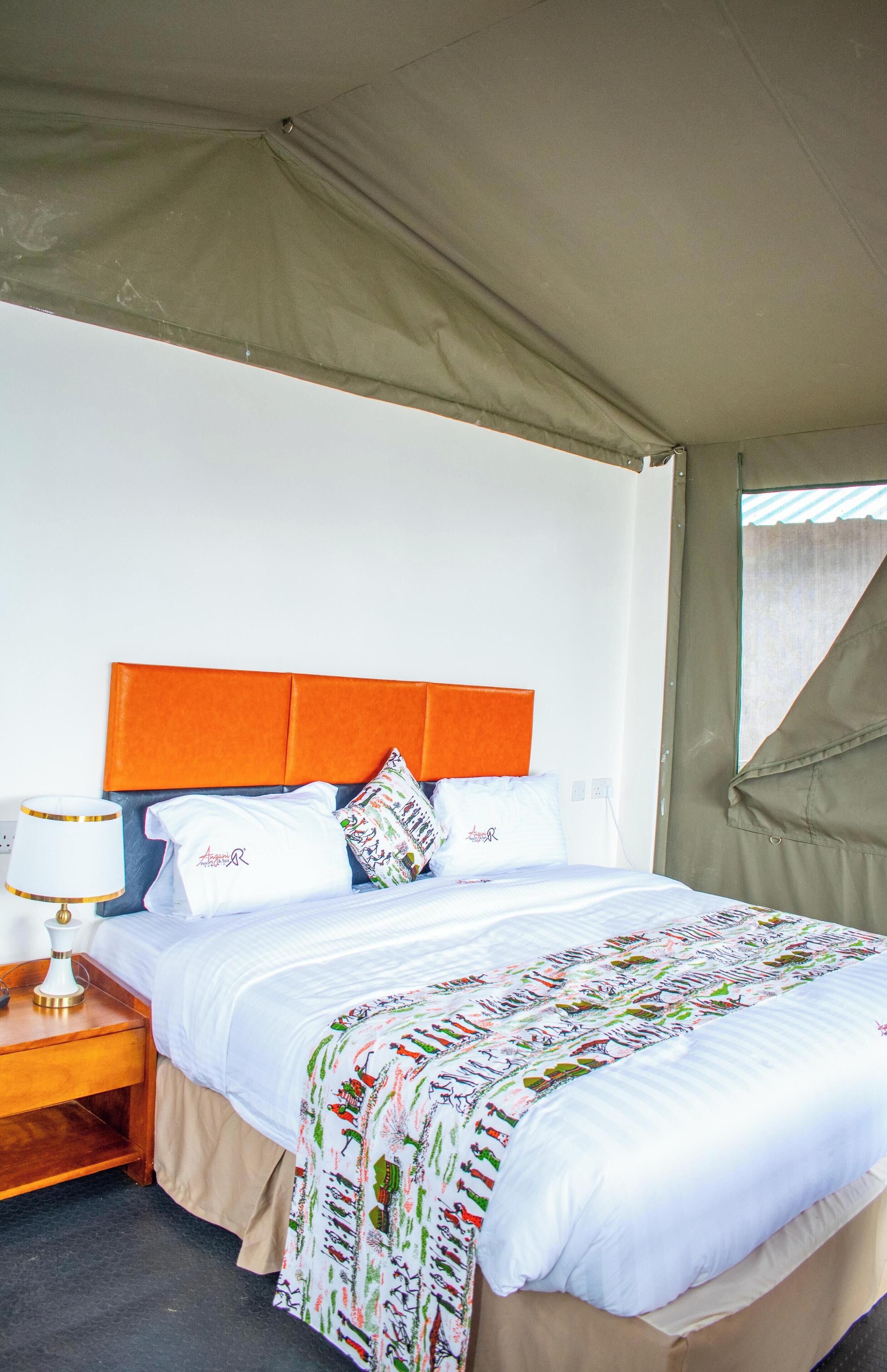 Un lit simple avec une tête de lit blanche et orange, une couvre-lit à motifs et une table de chevet avec une lampe.