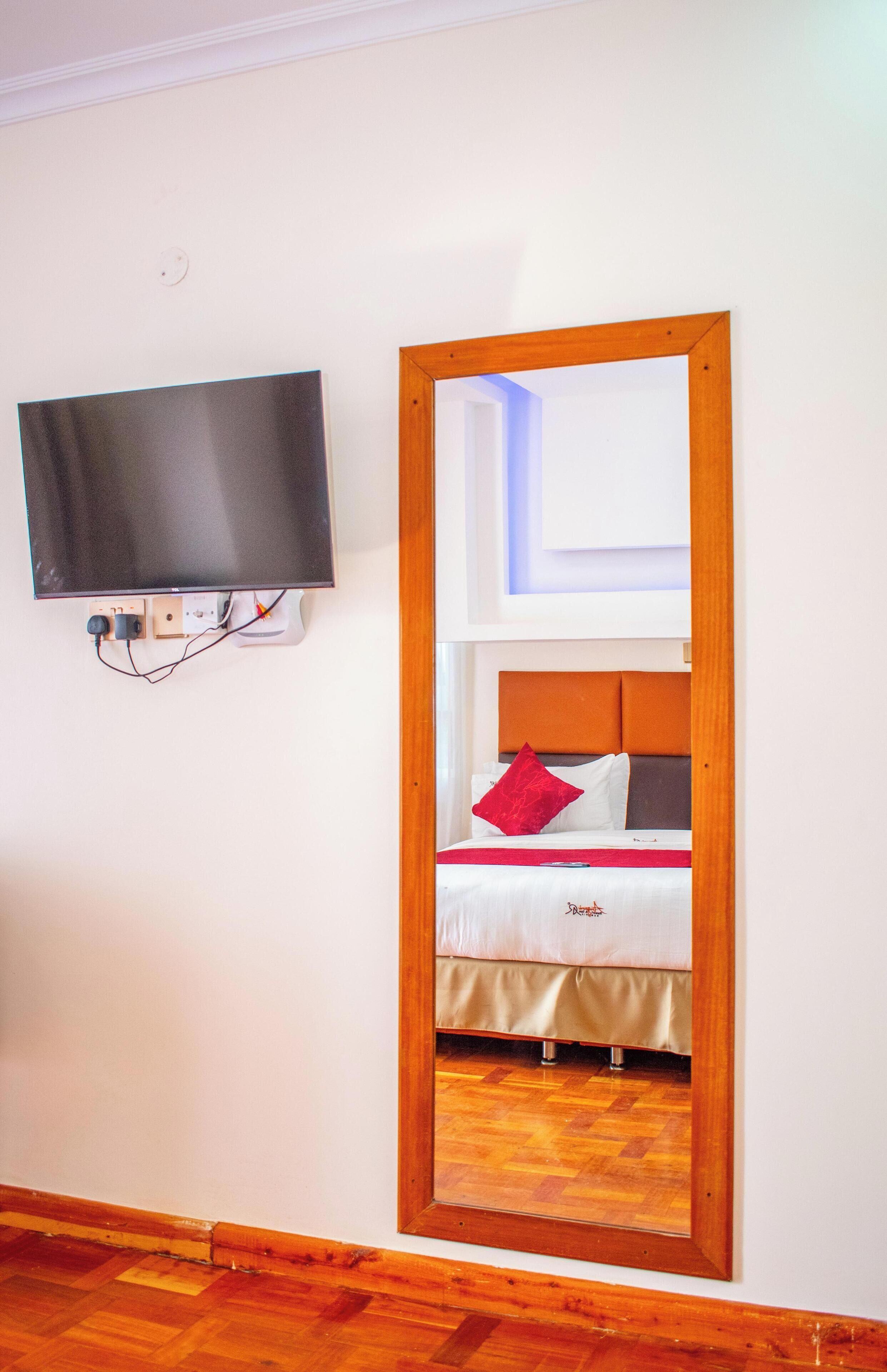 A room with a bed, a television mounted on the wall, and a mirror reflecting the bed and ceiling light.