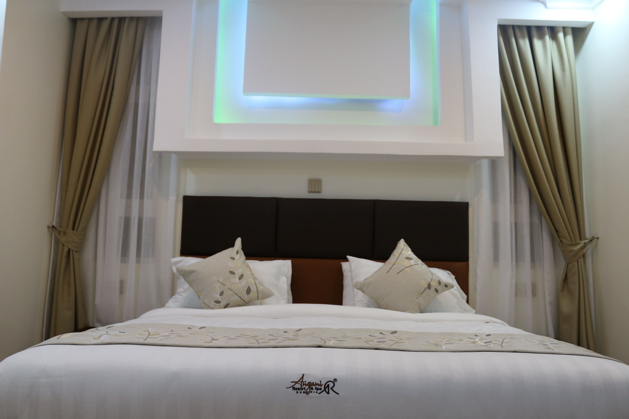 A neatly made bed with a floral bedspread, a headboard with a dark panel, and curtains on either side.