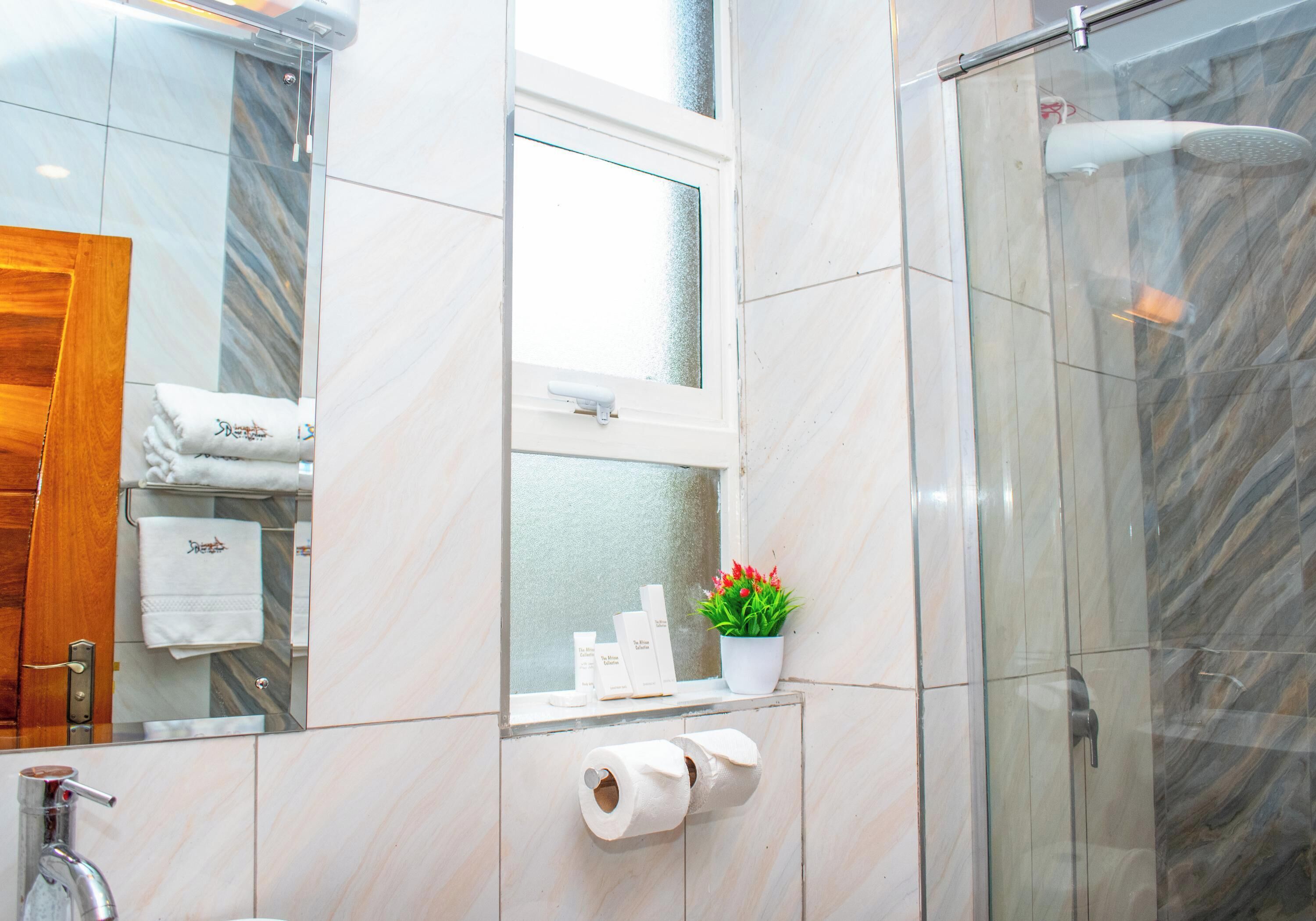Een badkamer met een glazen douchecabine, een spiegel, een handdoekhouder met handdoeken, een toiletpapierrolhouder en een potplant.