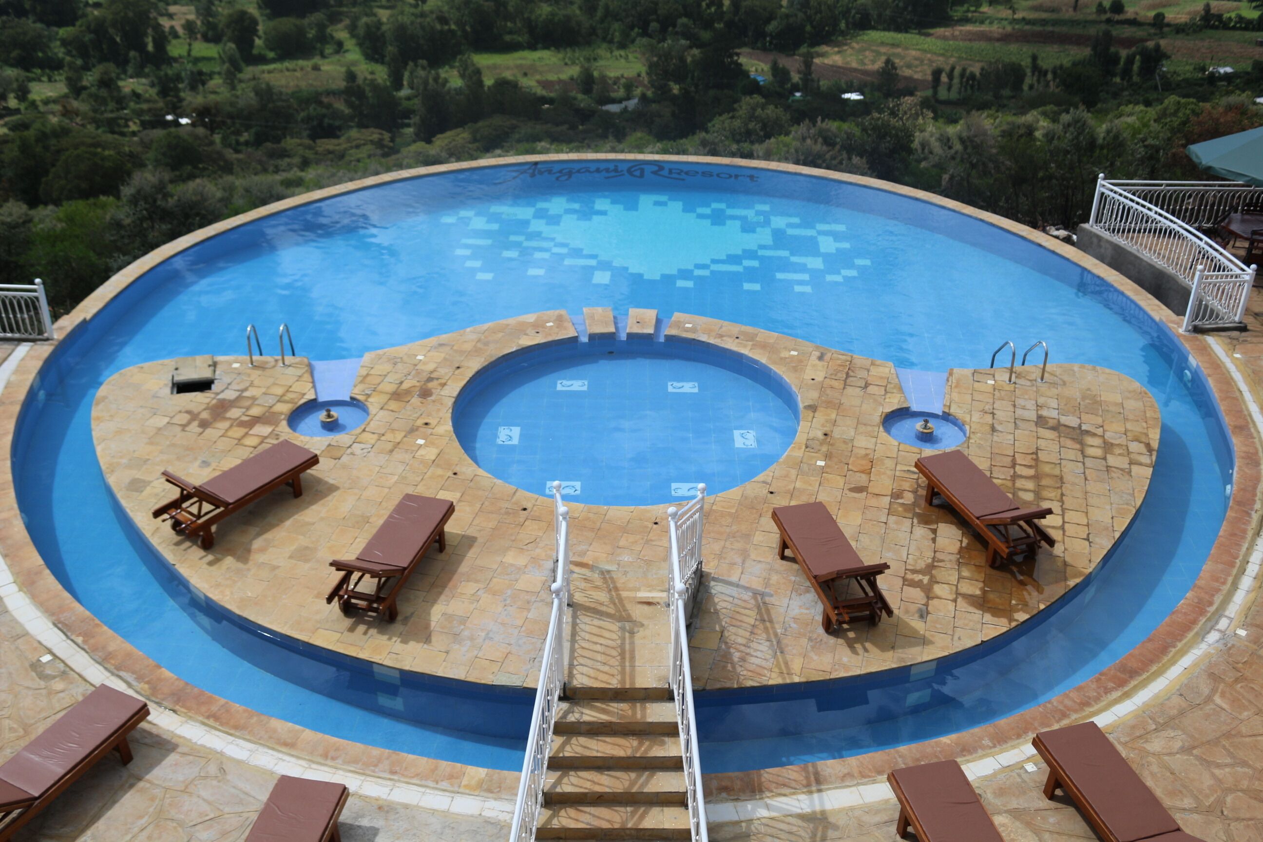 A circular swimming pool with a central hot tub, surrounded by lounge chairs and a stone deck.