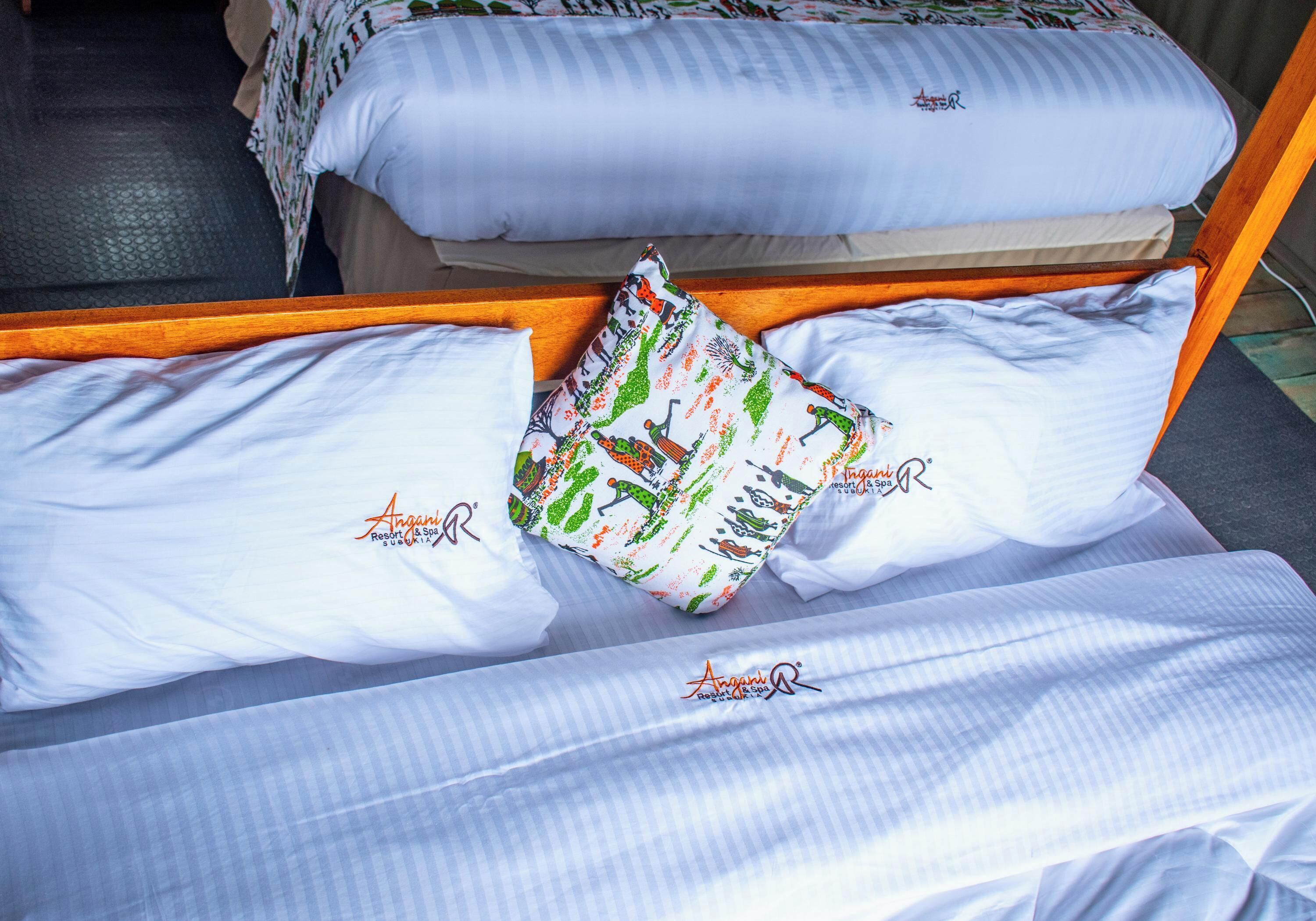 A bed with white linens and a colorful pillow.