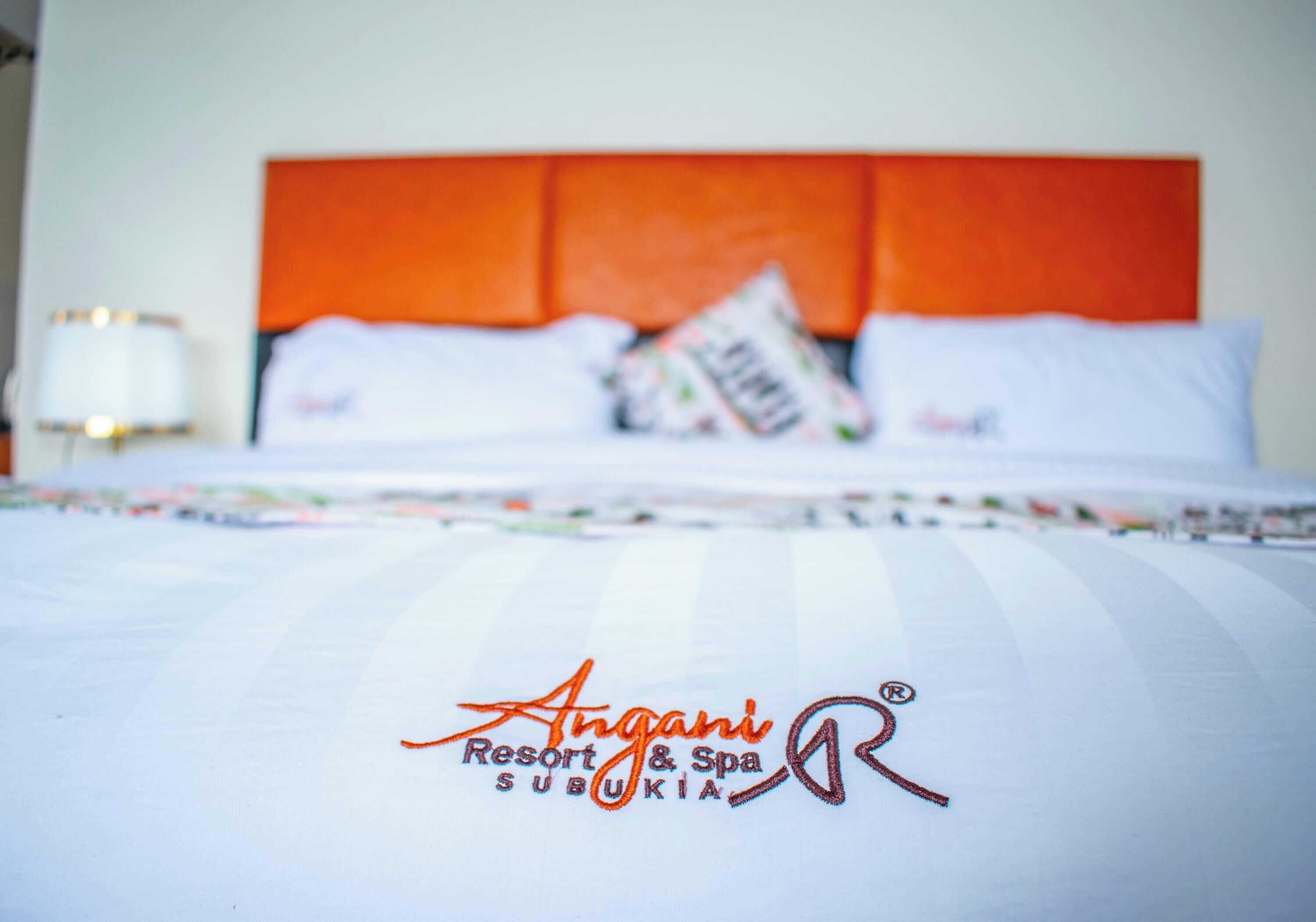 Una cama con cabecera blanca y naranja, el logo de Angani Resort & Spa, y una revista sobre la cama.