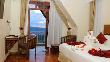 A hotel room with a balcony, a bed with a white swan decoration, and a desk with a chair.