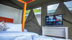 Quarto com cama, televisão em móvel e janela com vista para área verde.