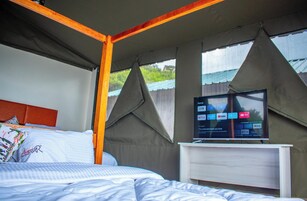 Un dormitorio con una cama, un televisor sobre un mueble bajo y un ventanal con vistas a zonas verdes.