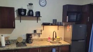 A compact kitchen with dark wooden cabinets, a microwave, a refrigerator, and a clock on the wall. - Craig's Coco Condo (Liberia)