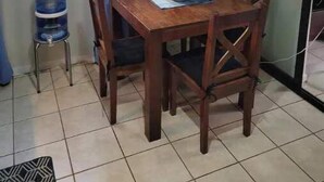 A dining area with a table and chairs, a water dispenser, and a window with curtains. - Craig's Coco Condo (Liberia)