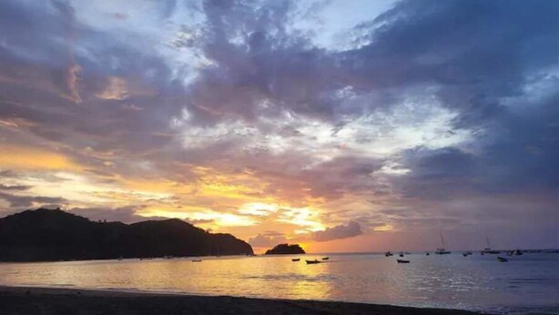 A sunset over a coastal area with boats and hills in the background. - Craig's Coco Condo (Liberia)