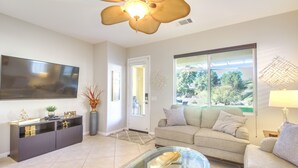 A modern living room with a flat-screen TV, a glass coffee table, a sofa, and a dining area with a cabinet. - 2 Mi to Empire Polo Club: Indio Home w/ Fireplace! (Indio)