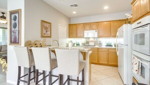 A modern kitchen with wooden cabinets, a white refrigerator, and a bar area with two chairs. - 2 Mi to Empire Polo Club: Indio Home w/ Fireplace! (Indio)