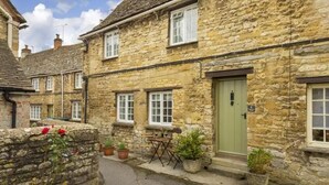 A stone building with a green door, windows, and a small outdoor seating area with plants. - Beautiful Historic High Street Cottage in Burford (Burford)