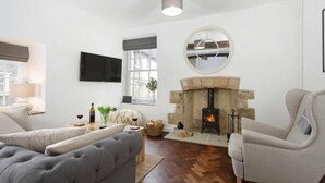 A modern living room with a fireplace, a television mounted on the wall, and comfortable seating. - Beautiful Historic High Street Cottage in Burford (Burford)