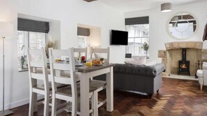 A cozy living room with a fireplace, a dining table with chairs, and a grey sofa. - Beautiful Historic High Street Cottage in Burford (Burford)