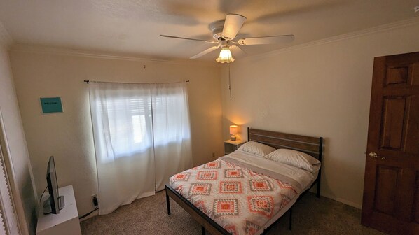 A bedroom with a bed, a ceiling fan, a bedside lamp, a window with curtains, and a door. - Charming retro home. Minutes from downtown and ERAU. Pet friendly. (Prescott)
