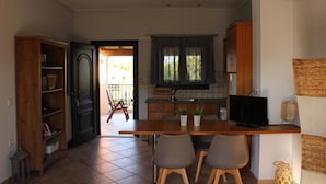 A compact kitchen with a dining area, wooden cabinets, a TV, and a window with curtains. - Panmar Villa 5 minutes from Saint Nicholas beach (Zakynthos)