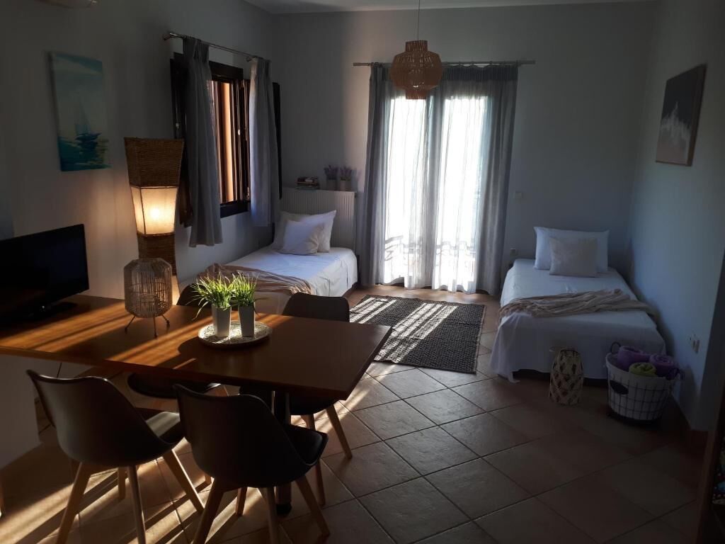 A hotel room with two beds, a dining table with chairs, a TV, a lamp, and a window with curtains.