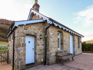 A stone building with two white doors, a bench, and a small porch area. - Railway Station Cottage (Presteigne)