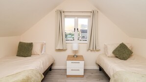 Une chambre avec deux lits, une table de chevet, une fenêtre avec des rideaux et une vue sur les bâtiments à l’extérieur.