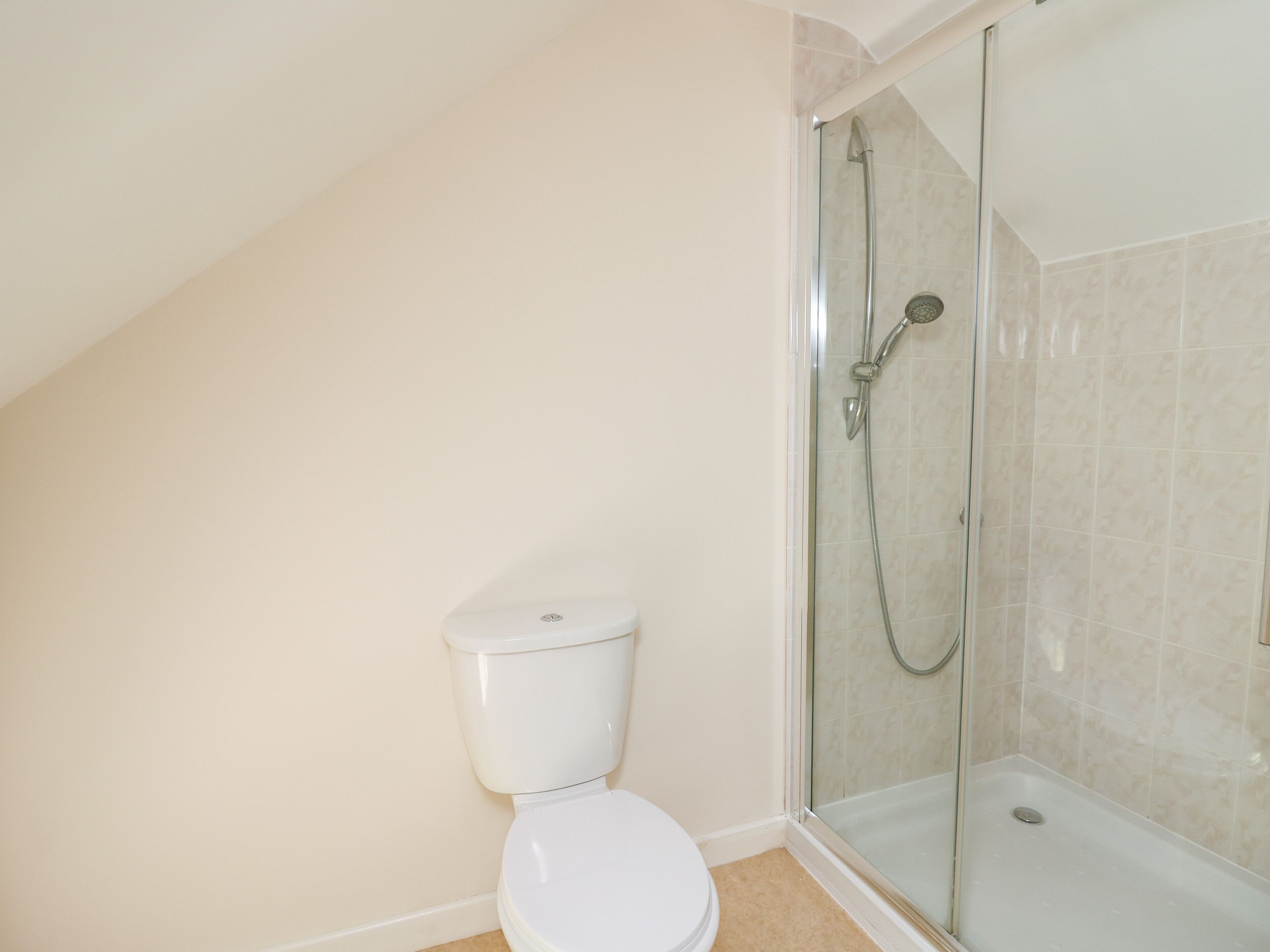 A bathroom with a toilet, a glass-enclosed shower, and beige walls.