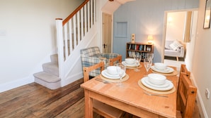 Un coin repas avec une table en bois dressée pour quatre personnes, une chaise à carreaux, une bibliothèque et un escalier.