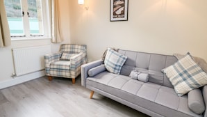 Un salon chaleureux avec un canapé gris, un fauteuil à carreaux et un tableau encadré au mur.