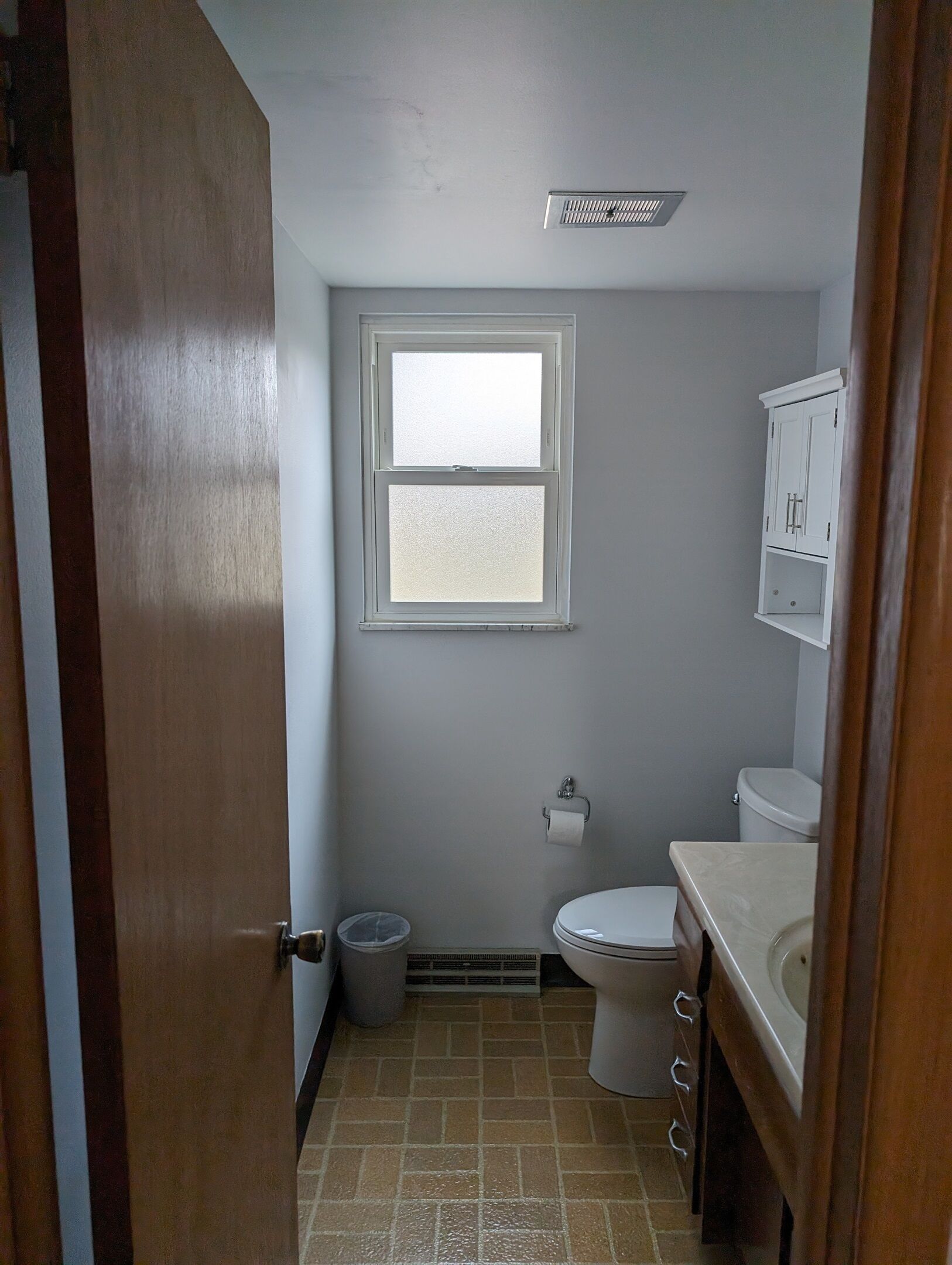 A small bathroom with a toilet, sink, and window.