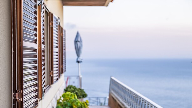 A balcony with metal shutters, a potted plant, and a view of the sea. - White Rabbit I by Madeira Sun Travel (Calheta)
