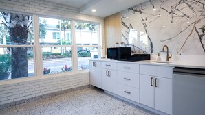 A modern kitchen with white cabinets, a marble backsplash, and a large window overlooking a street. - Ivory Sands Beach Suites - Standard King (Clearwater)