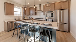 A modern kitchen with a central island, bar stools, stainless steel appliances, and pendant lighting. - Ski&Tee Mountain Chalet: modern retreat w/ golf simulator, hot tub, & game room (Park City)