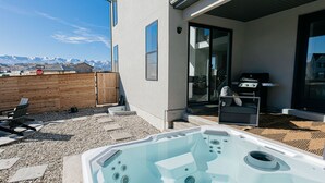 A modern outdoor area with a hot tub, a barbecue grill, and a view of snow-capped mountains. - Ski&Tee Mountain Chalet: modern retreat w/ golf simulator, hot tub, & game room (Park City)