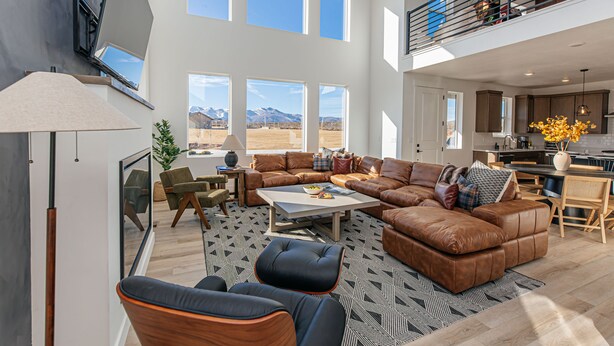 A spacious living room with a large sectional sofa, a coffee table, and a dining area with a kitchen in the background. - Ski&Tee Mountain Chalet: modern retreat w/ golf simulator, hot tub, & game room (Park City)