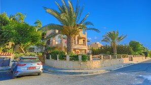 A residential area with a parked car, a palm tree, and a building with balconies. - 3 Bedroom Villa, Private Pool, 250m to Latchi Beach (Latchi)